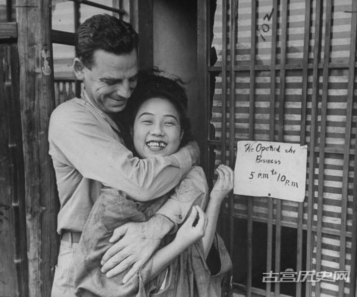 钉扎标志门的艺妓女孩被一个美国陆军士兵男子抱住，摄影师借两人的照片有意无意间透露出了战后日本与美国的关系。地点是日本东京，1945年10月，摄影师：乔治·Silk。