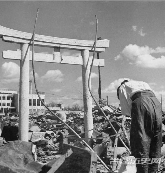 一个日本女人站在神社牌坊前她家的废墟之中为她被燃烧弹烧死的丈夫鞠躬祈祷。