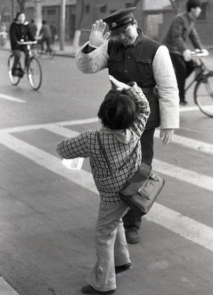 1981年北京西四街头。画面中的警察是西四交通支队交警，他每天在此路口护送小学生过马路。每当送过一拨小学生后，被护送的学生就会向警察叔叔敬礼表示感谢。