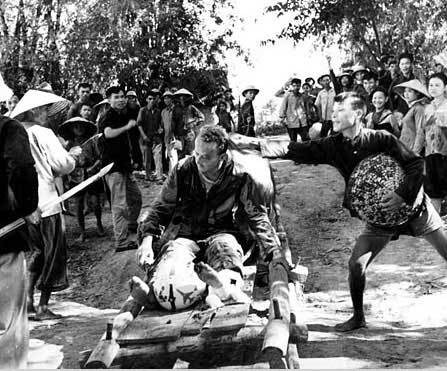 越南战争，简称越战，又称第二次印度支那战争。战争中，美军利用空中优势，多次派出战机对越南进行轰炸。图为越南村民在羞辱腿部受伤被俘的美国空军飞行员Willard S.Giedon(1966.8.7)