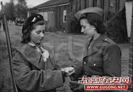 一名前德国女军官，战后于1945年9月获得释放，正在向看守集中营的背枪盟军女兵出示释放证。女军官的军衔、肩章、领章等都已被除去，低着头，神态谦卑，想来是在集中营里“表现良好”。